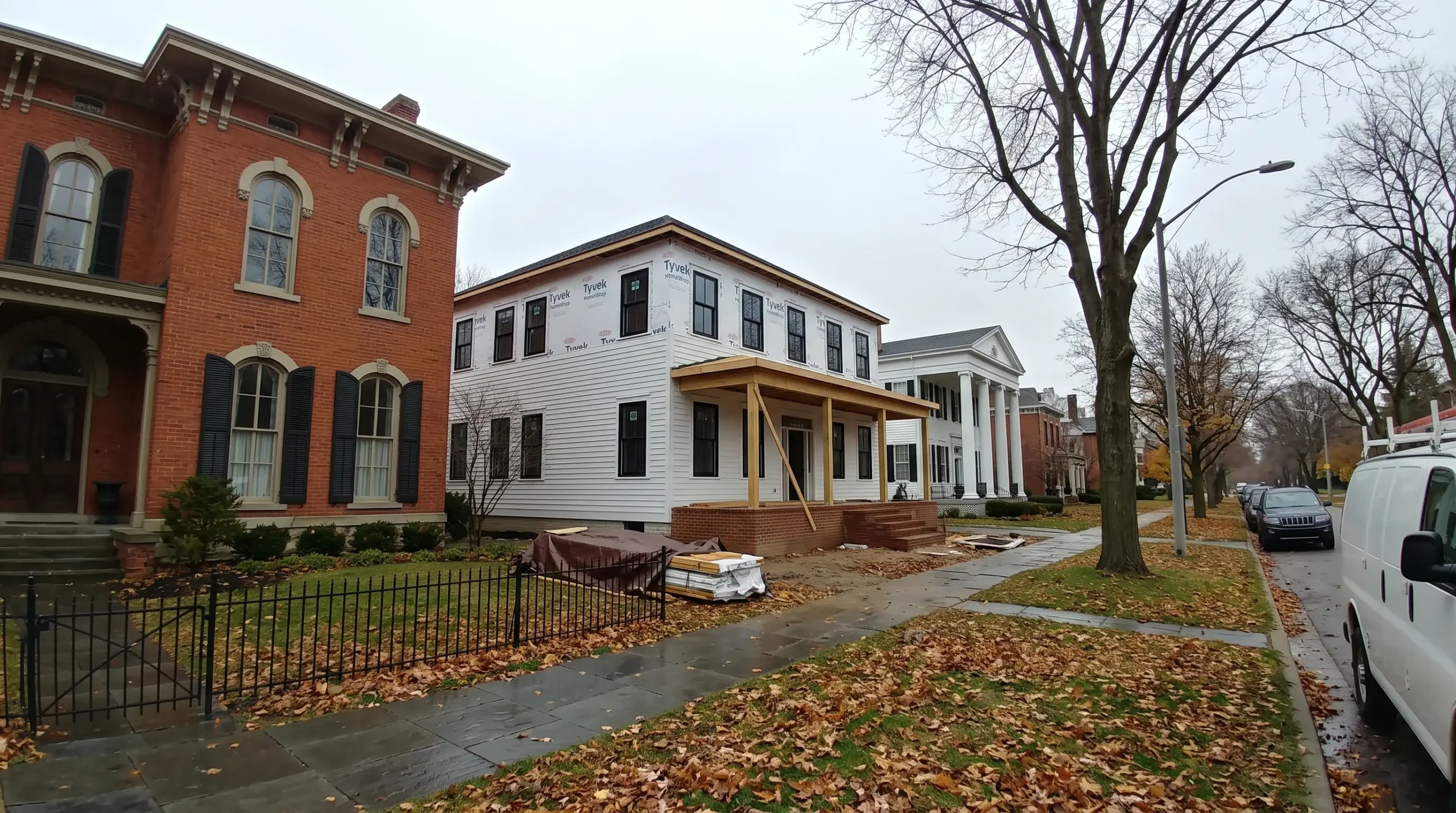 A new traditional home with clapboard siding going up between a brick Italianate house and a columned white house on a street of mature trees